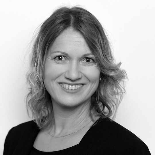 Porträt von Claudia Hempel. Sie hat schulterlanges, welliges, blondes Haar und trägt ein dunkles Oberteil mit einem dezenten Kettchen. Sie lächelt freundlich in die Kamera, vor einem hellen Hintergrund.