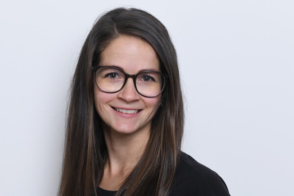 Porträt von Sindy Harka. Sie trägt eine dunkle Brille und hat lange, glatte, dunkelbraune Haare. Sie lächelt leicht in die Kamera. Der Hintergrund ist hell.