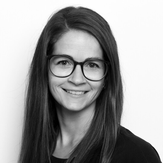 Porträt von Sindy Harka. Sie trägt eine dunkle Brille und hat lange, glatte, dunkelbraune Haare. Sie lächelt leicht in die Kamera. Der Hintergrund ist hell.